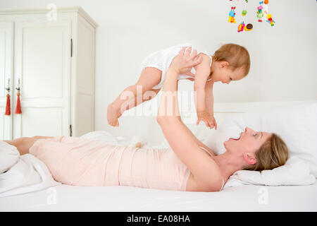 Mother lifting baby daughter on bed Stock Photo