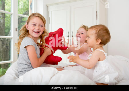 Three girls playing on bed with soft toy Stock Photo