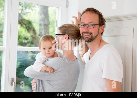 Mother and father looking out of window with baby daughter Stock Photo