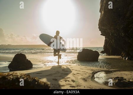 Mature man running towards sea, holding surf board Stock Photo