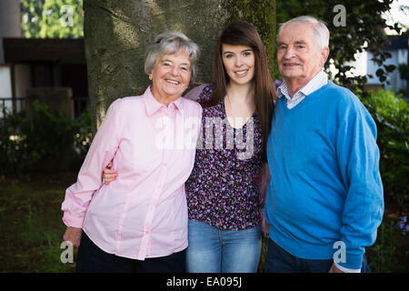 Grandparents and granddaughter standing by tree Stock Photo