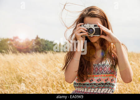 Young woman taking photo with vintage camera in field Stock Photo