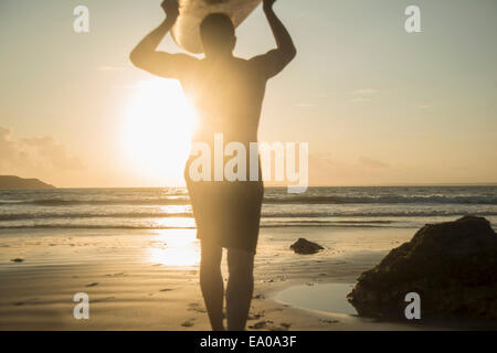 Mature man, walking towards sea, holding surf board Stock Photo