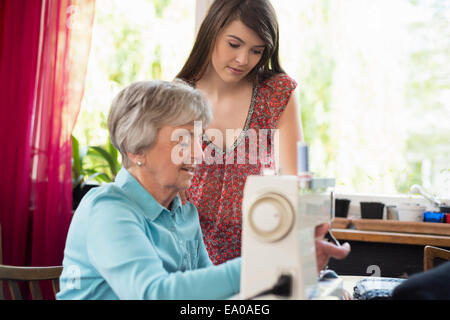 Granddaughter watching grandmother use sewing machine Stock Photo