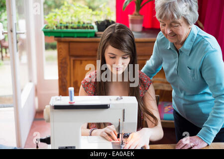Senior woman watching granddaughter use sewing machine Stock Photo