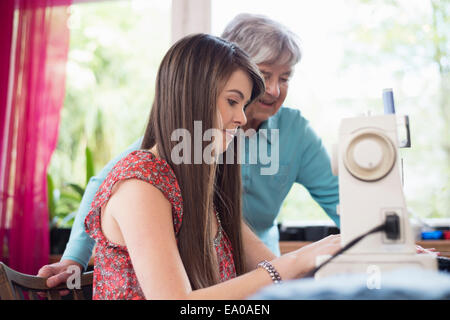 Senior woman watching granddaughter use sewing machine Stock Photo