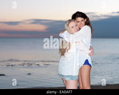 Portrait of two young women friends hugging on beach at dusk, Williamstown, Melbourne, Australia