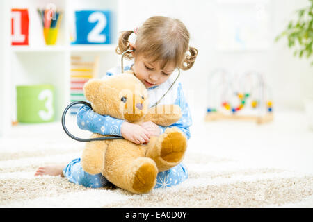 Cute little girl playing doctor with plush toy at home Stock Photo