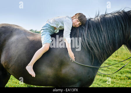 Cropped shot of boy leaning forward with eyes closed on horse in field Stock Photo