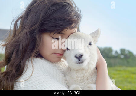 Portrait of young woman in field carrying lamb wrapped in blanket Stock Photo