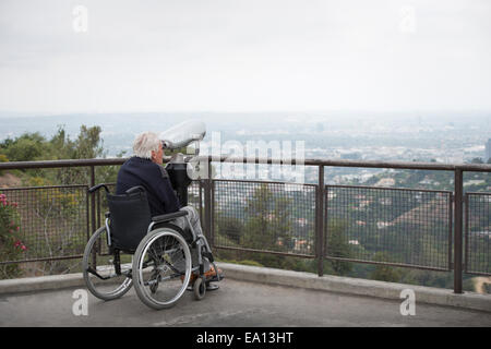 Senior man in wheelchair looking at city through coin operated binoculars from viewing balcony Observatory Griffith Park Los Stock Photo