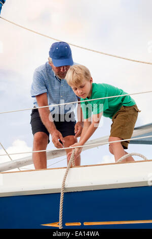 Boy helping grandfather pull ropes on sailboat Stock Photo