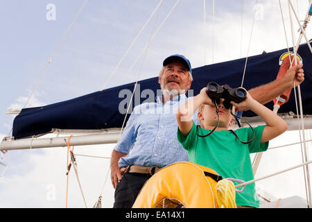 Boy and grandfather on sailboat looking through binoculars Stock Photo