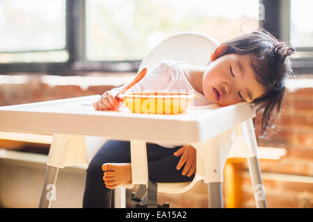 One year old baby girl asleep in highchair at breakfast Stock Photo