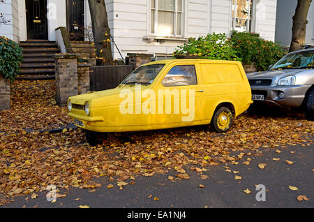 A bright yellow Reliant Robin classic car parked in a leafy street. Stock Photo