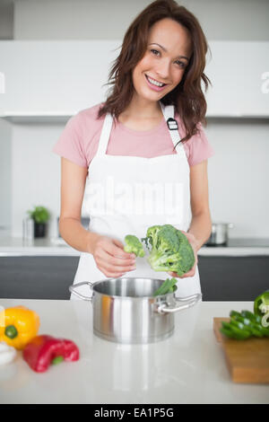 Smiling young woman with broccoli in kitchen