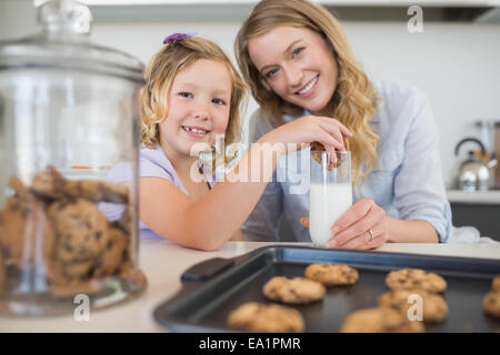 Mother with girl dipping cookie in milk Stock Photo