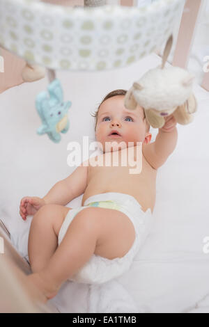Adorable baby playing with toys in crib Stock Photo