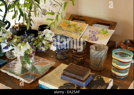 Row of glass cups on table top with small watercolours and vase of sweet pea flowers. Stock Photo