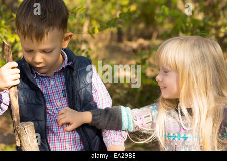 Boy and Girl Playing Together with Stick Outdoors in Autumn Stock Photo