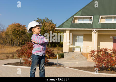 Serious Cute Male Engineer Kid in White Helmet. Captured Outside the House Facing to His Left Side. Stock Photo