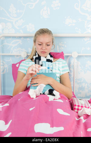 Sick teen girl laying in bed with thermometer for the temperature Stock Photo