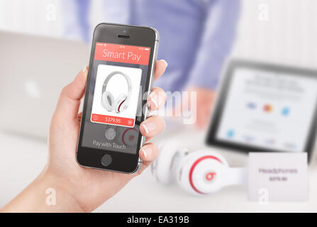 Woman is buying headphones by black mobile smart phone with nfc smart pay application on the screen. Blurred store with differen Stock Photo