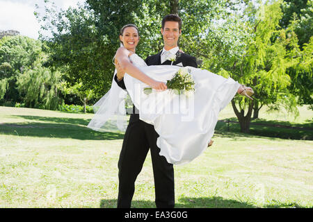 Young groom lifting bride in arms at garden Stock Photo