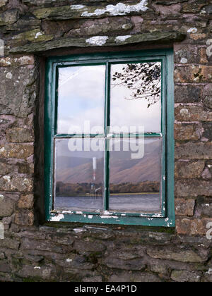 Reflections of Loweswater lake and mountains in old window of Holme Wood Bothy, Loweswater, Lake District, Cumbria, England, UK Stock Photo