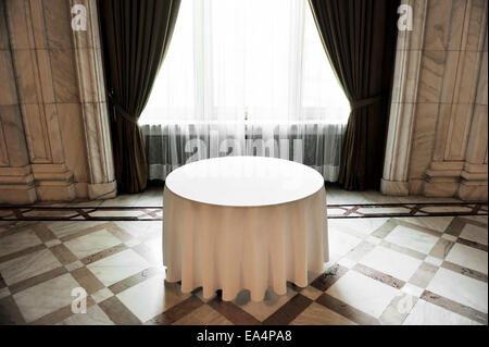 Sunlight falls on an empty round dinner table in a festive marble room Stock Photo