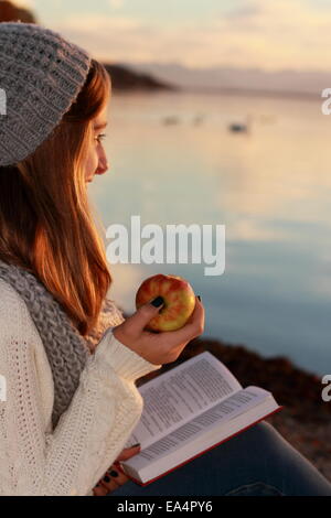 Happy girl sitting with book and apple on sunset Stock Photo