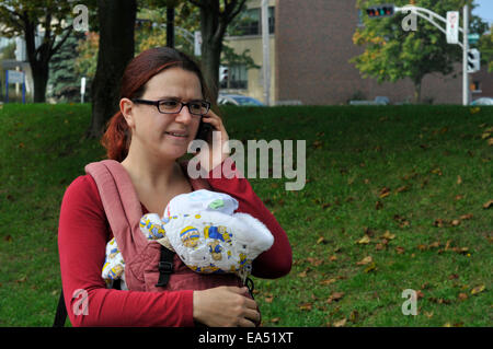 A mother carrying a baby and using a mobile phone Stock Photo