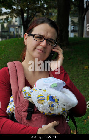 A mother carrying a baby and using a mobile phone Stock Photo