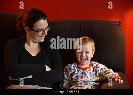 Mother and son in pyjamas, sat laughing together on a sofa Stock Photo