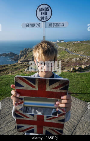 UK, Cornwall, boy taking a selfie in front of direction sign at Land's End with his digital tablet Stock Photo