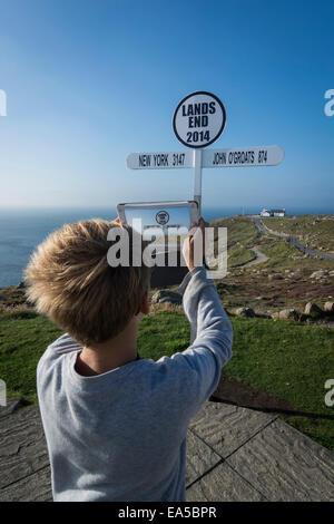UK, Cornwall, boy photographing direction sign at Land's End with his digital tablet Stock Photo