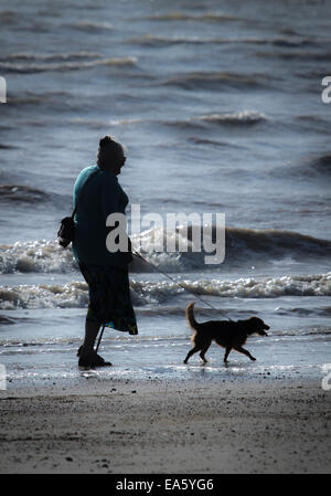 A silhouette of an elderly lady walking her dog along the beach at Littlehampton, West Sussex. Stock Photo