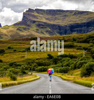 UK, Scotland, Woman with umbrella on country road Stock Photo