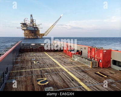 Nautical vessel approaching an oil platform at sunrise Stock Photo