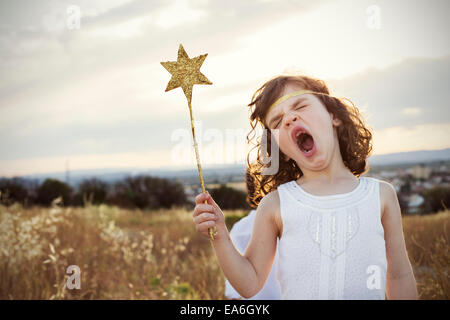 Girl dressed as a fairy holding a magic wand standing in a meadow yawning Stock Photo