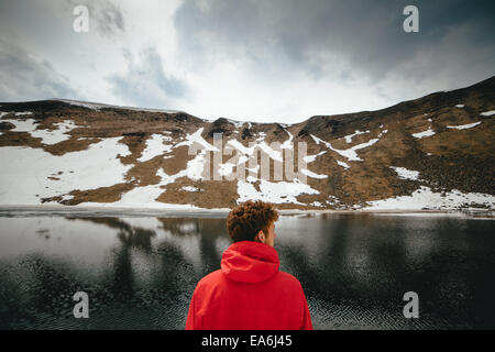 Back view of young man looking at mountain lake Stock Photo