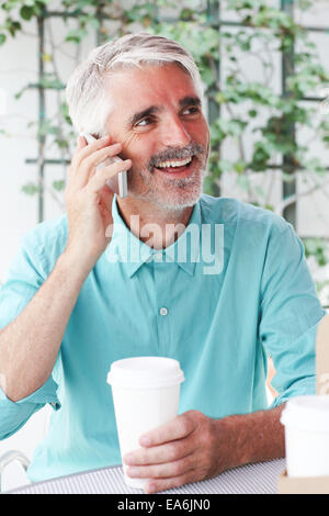 Businessman with coffee cup in hand talking on phone in sidewalk cafe Stock Photo