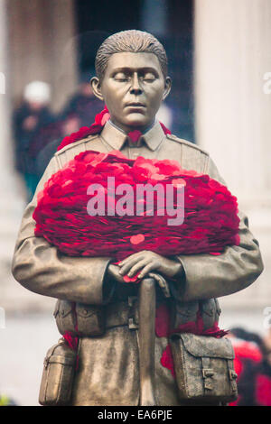 Trafalgar Square, London, UK. 7th November, 2014. The Royal British Legion unveiled the Every Man Remembered sculpture in Trafalgar Square, a collaborative piece with the artist Mark Humphrey. The brass sculpture, loosely based on the Unknown Solider, stands on a plinth of limestone sourced from the Somme and is encased in a Perspex obelisk, surrounded by poppies which float up around the figure every five minutes. PICTURED: Cradled in his arms, a precious burden of poppies. Credit:  Paul Davey/Alamy Live News Stock Photo