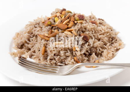 Lebanese spiced rice with minced beef and garnished with freshly toasted nuts on a plate with a fork Stock Photo