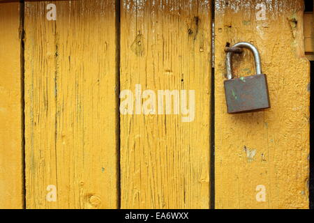 old metallic padlock on yellow wooden door, interesting textured view Stock Photo