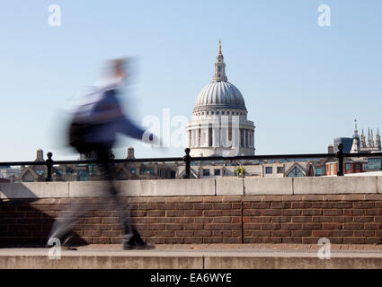 A view of the dome of Saint Pauls Cathedral across the River Thames with motion blurred businessman walking in the foreground Stock Photo