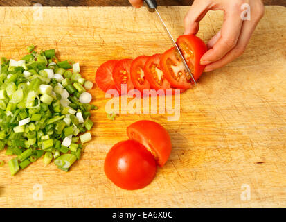 woman slicing tomatoes and chopped spring onions on a wooden chopping board Stock Photo