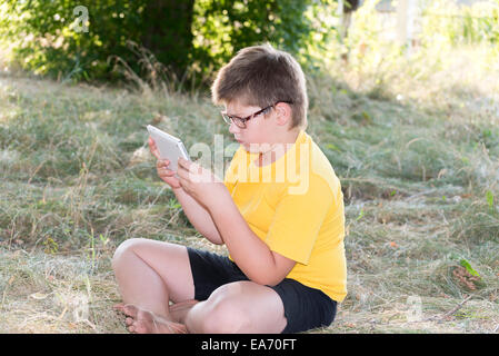 The boy in glasses looks tablet computer at nature Stock Photo