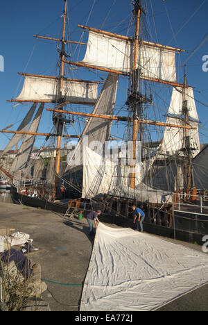 two men working on re rigging the sails of a tall ship moored at Charlestown harbour Cornwall Stock Photo