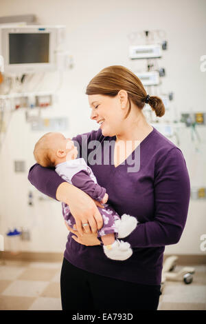 Mother standing in hospital ward holding baby son (6-11 months) Stock Photo